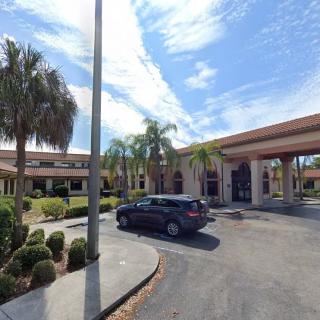 A parking lot in front of a building surrounded by palm trees under a cloudy sky.