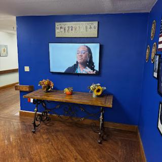 A cozy living room corner featuring a blue wall, a wooden table with decorative items, and a television displaying content.