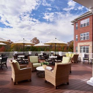 An inviting outdoor patio area with wicker chairs and tables under large umbrellas, set against a backdrop of a brick building and a partly cloudy sky.