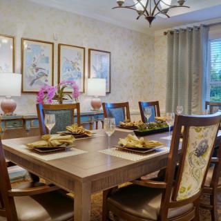 A well-decorated dining room with a large table set for a meal, surrounded by elegant chairs and adorned with artwork and soft lighting.