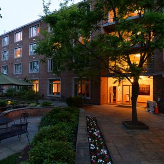 A well-lit apartment building with a brick exterior surrounded by trees and neatly maintained landscaping during the evening.