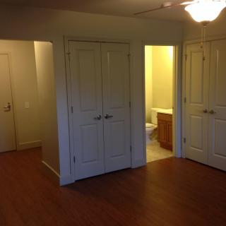 A view of an apartment interior with a closet, bathroom, and wood flooring.