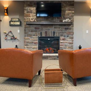 A cozy living room with two armchairs facing a fireplace and a television mounted on the brick wall.