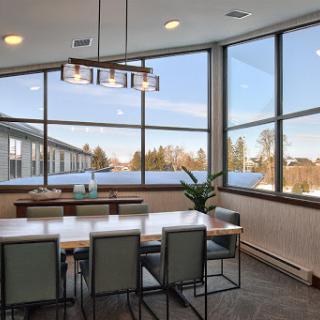 A modern dining area featuring large windows that invite ample natural light, complemented by stylish furniture and plant decor.