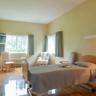 A bright hospital room with a bed, table, and chairs near a window.