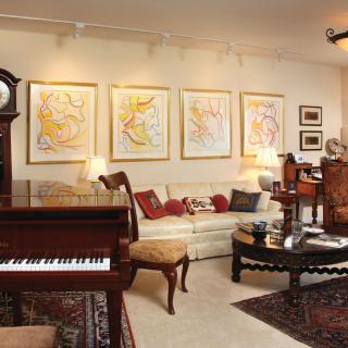 A cozy living room with classical furnishings, featuring a grand piano, elegant artwork on the walls, and a decorative rug.