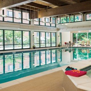 A serene indoor swimming pool area with large windows allowing natural light to fill the space, complemented by a relaxation spot with towels laid out.
