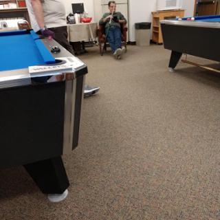 A view of a recreational game room featuring pool tables and a person seated in the background.