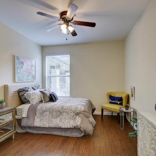A cozy bedroom with modern decor, featuring a comfortable bed, ceiling fan, and a bright window.