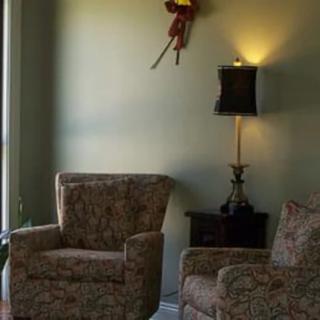 A cozy living room with two chairs, a side table, and a lamp under wall art.