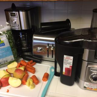 A kitchen counter with a juicer, toaster, and coffee maker alongside chopped fruits and vegetables.