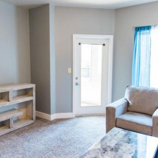 A cozy living room with a comfortable armchair, built-in shelves, and ample natural light streaming in through the window and door.