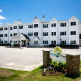 Front view of a white hotel building with a welcoming sign and clear blue sky.
