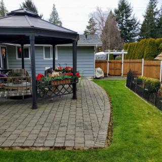 A backyard view featuring a gazebo and patio with outdoor seating, surrounded by a well-maintained lawn and a wooden fence.