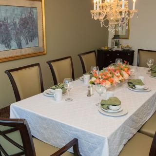 A dining room with a neatly arranged table, featuring a floral centerpiece and elegant place settings under a chandelier.