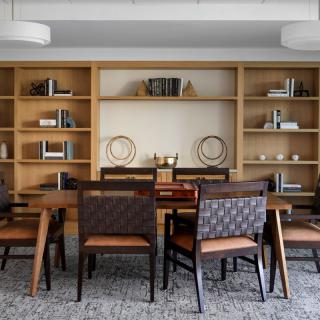 A modern dining room with a wooden table, upholstered chairs, and built-in shelving.