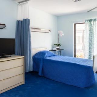 A hospital room with a single bed, television, and blue decor.