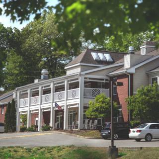 A two-story building with balconies surrounded by trees and parked cars.