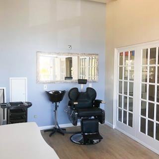 A well-lit salon interior featuring a barber chair, large mirror, and hairdressing equipment.