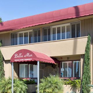 Apartment building entrance with a red awning and surrounding greenery.
