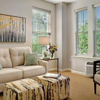 A cozy living room with a sofa, artwork, and ample natural light streaming through the windows.