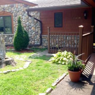 A beautiful house exterior with a stone wall and wooden siding, featuring a well-maintained garden and potted plants.