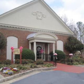 A brick building with a decorative entrance adorned with a wreath, surrounded by well-maintained landscaping and a red carpet leading to the door.