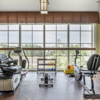 A modern gym with exercise equipment including a treadmill and stationary bike, featuring large windows with a view.