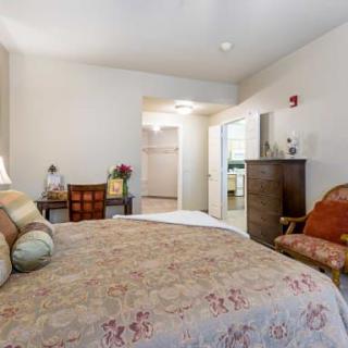 A cozy bedroom with a large bed, wooden dresser, and upholstered chair.