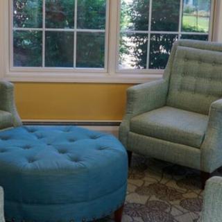 A cozy living room setup with two armchairs and a round ottoman near large windows.