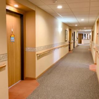 A well-lit hospital corridor with doors and carpeted floor.