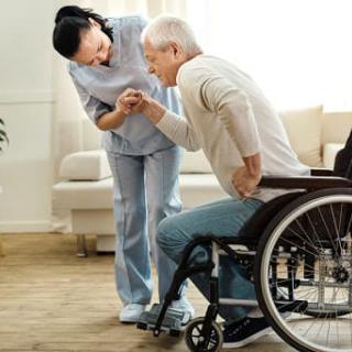 A nurse assisting an elderly man in a wheelchair at home, providing support and care.