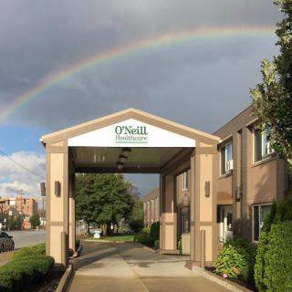 A beautiful rainbow arcs over the entrance of the O'Neill building against a cloudy sky.