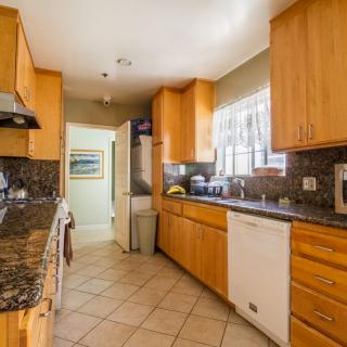 A modern kitchen with wooden cabinets and granite countertops features appliances and a tiled floor.
