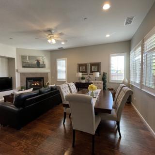 A spacious living and dining area with modern decor, featuring a ceiling fan and large windows.