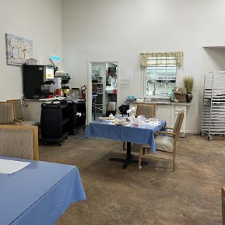 A spacious dining area featuring neatly set tables with blue tablecloths, adjacent to a kitchen setting.