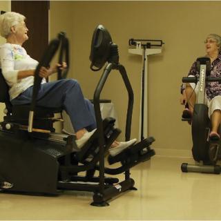 Two seniors exercising on fitness equipment indoors, promoting health and wellness.