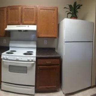 A small kitchen area featuring a stove, refrigerator, and wooden cabinets.