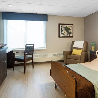 A well-lit hospital room with a bed, chair, desk, and window.