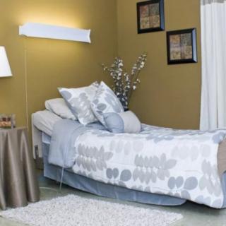 A modern bedroom with stylish decor, featuring a neatly made bed with patterned pillows, a lamp on the nightstand, and framed wall art.