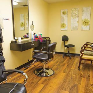 A cozy hair salon interior with styling chairs and a mirror, featuring wooden flooring and salon equipment.