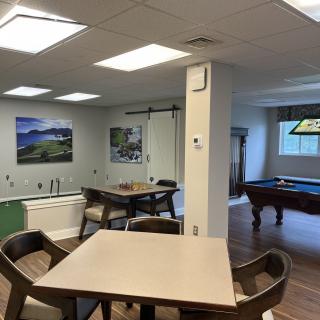 A well-lit recreation room featuring a pool table, tables, and chairs for leisure activities.
