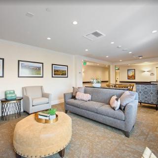 A modern living room with a cozy gray sofa, an armchair, and a round coffee table, decorated with artwork and ambient lighting.