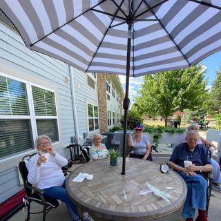 A group of seniors enjoying a sunny day outdoors under an umbrella, sharing laughter and conversation.