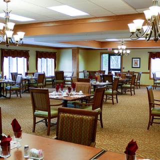 A spacious dining room with neatly arranged tables and chairs, well-lit by elegant chandeliers.