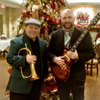 Two musicians posing together in front of a beautifully decorated Christmas tree.
