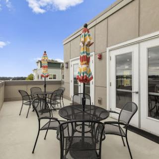 A spacious rooftop patio featuring stylish outdoor furniture, colorful umbrellas, and a bright blue sky.