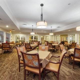 A spacious dining room with neatly arranged tables and chairs, illuminated by elegant chandeliers.