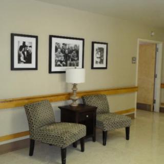 A hallway with patterned chairs and a table, adorned with framed black and white photos on the wall.