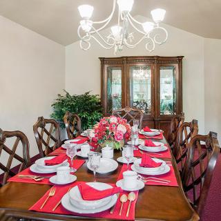 An elegantly set dining table with red placemats and a floral centerpiece, illuminated by a chandelier.